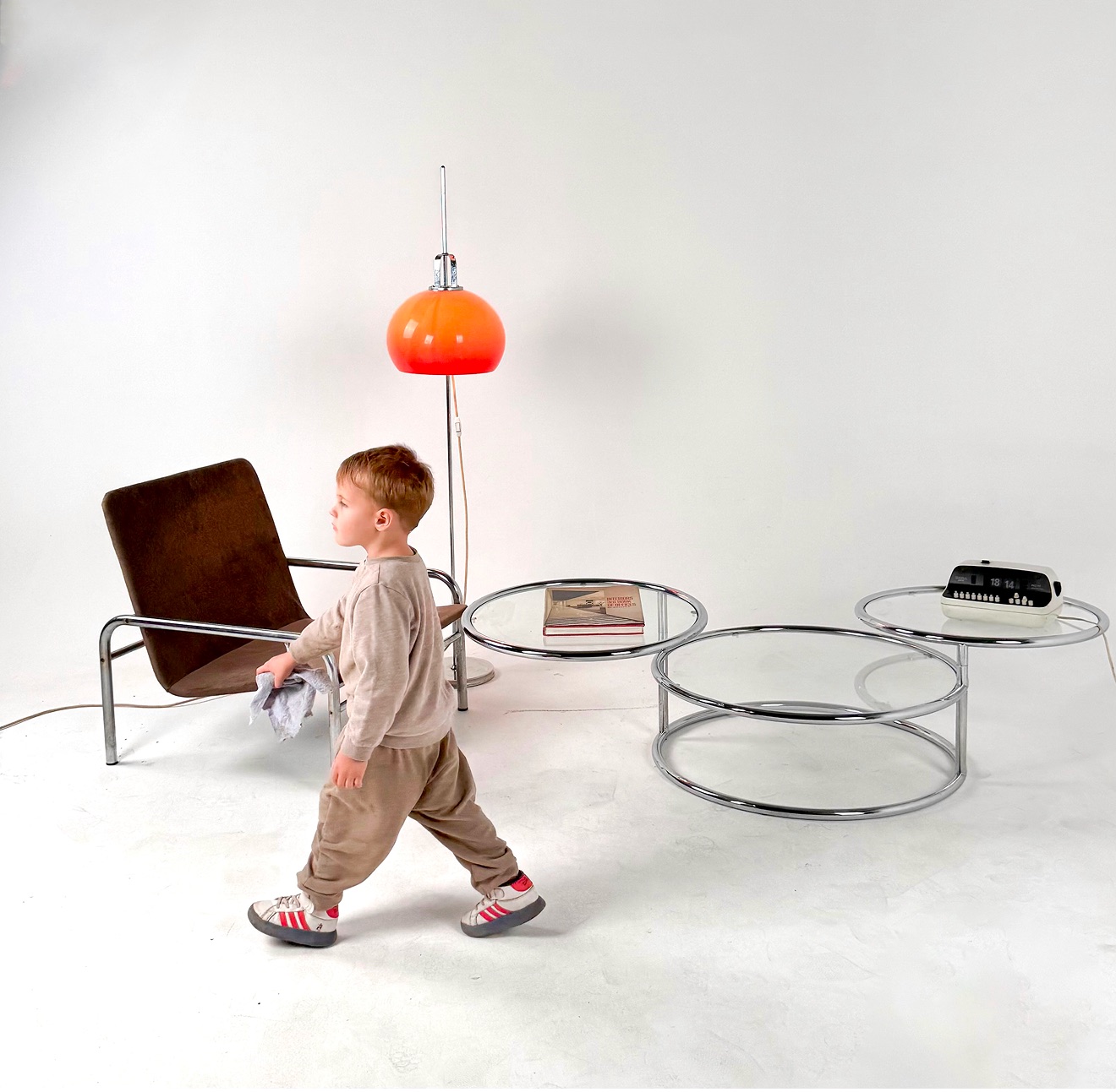 Round chrome-and-glass tables and a brown suede tubular armchair under an orange mushroom lamp