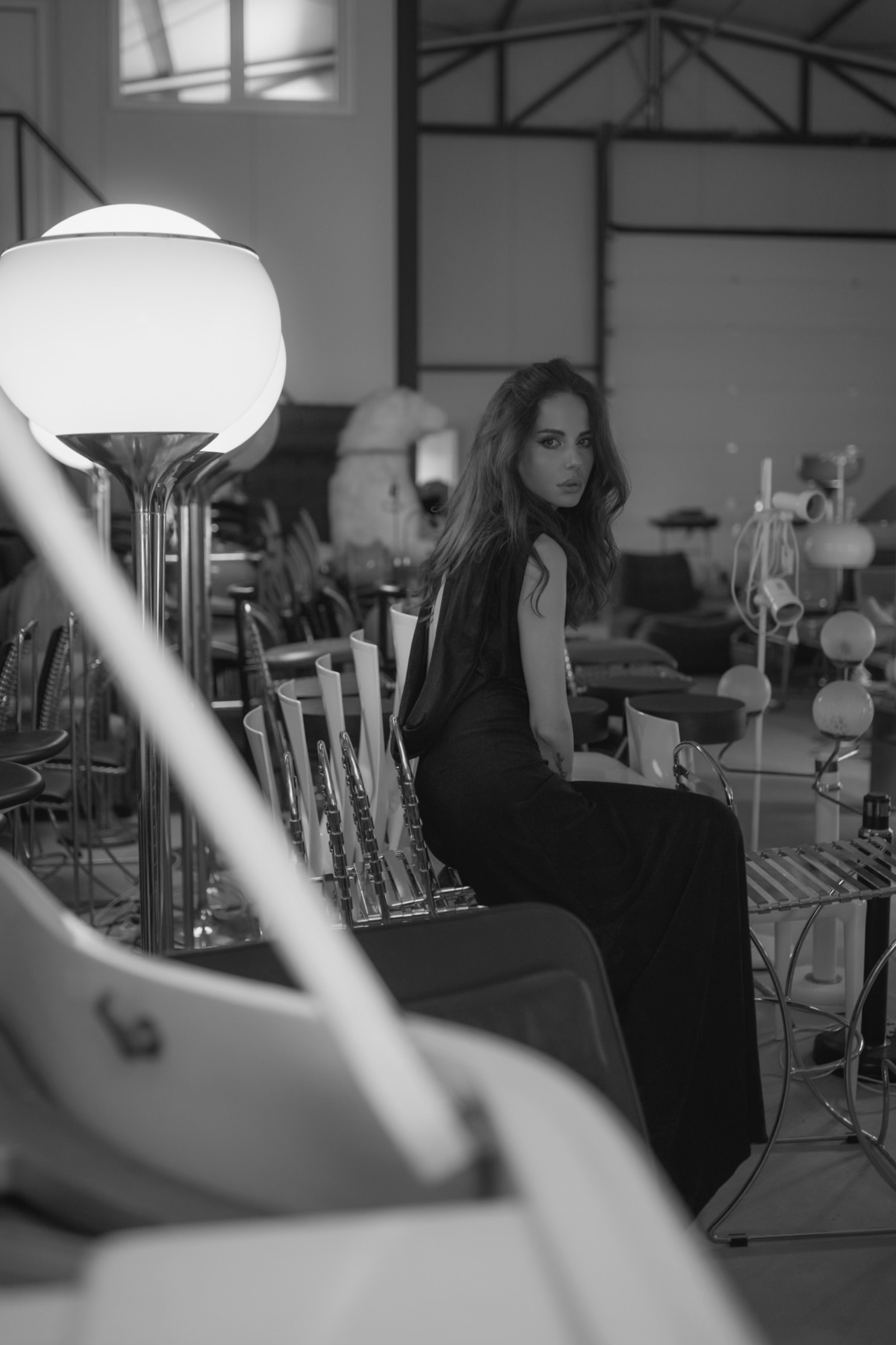 Model seated among vintage lamps, chairs and designer props in the Studio SPACE prop archive