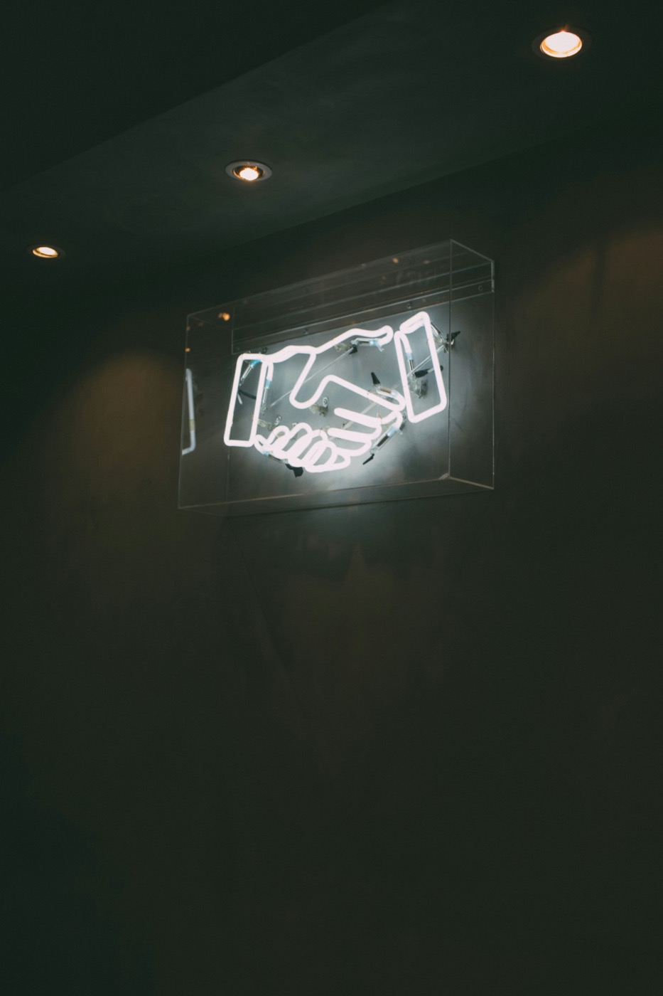 Neon handshake sign glowing in a dark room