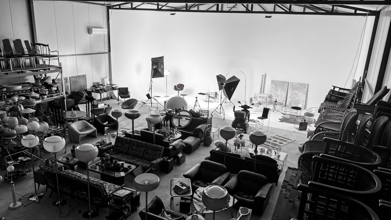 The studio floor seen end to end, filled with props, furniture and lighting stands.